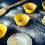 From above of yellow cupcake molds and cooking utensils placed on dirty table with flour